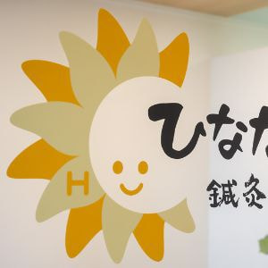ひなたぼっこ鍼灸・整骨院のロゴマーク。ひまわりのような笑顔の太陽が印象的なデザイン。